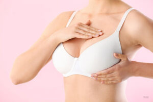 cropped image of woman's torso in white bra, massaging her breast with two hands