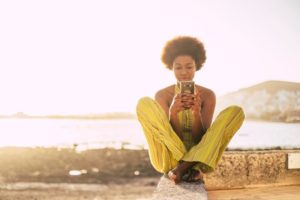 Woman sitting near coast on her cell phone.