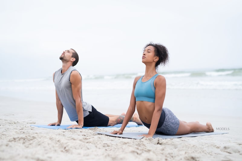 Man and woman doing yoga stretches on the beach