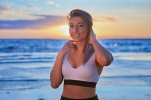 Woman in white baking suit standing on beach at sunset