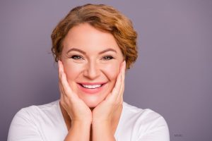 Beautiful mature woman smiling while placing her hands on either side of her face.